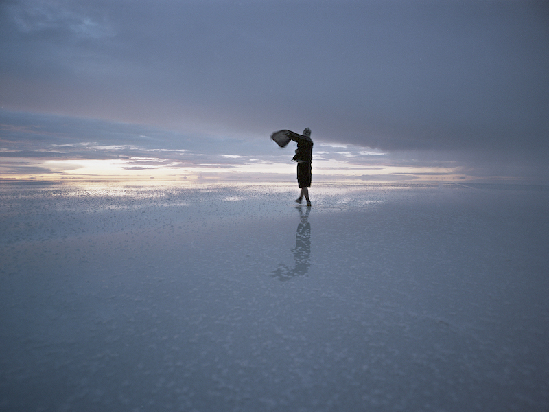 The sillhouette of a person dancing on a beach at dusk.